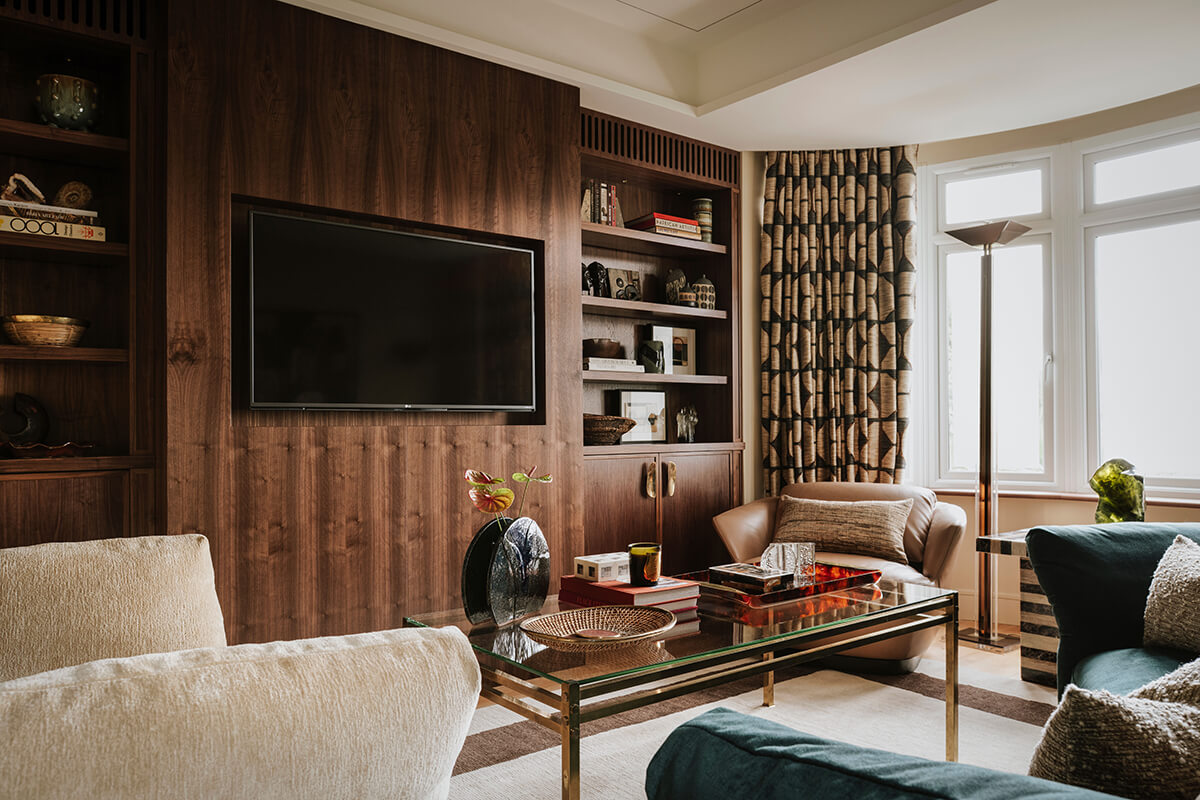 Deep teal sofa styled with walnut timber panelling and layered neutral textures in Alex Dauley's London living room.