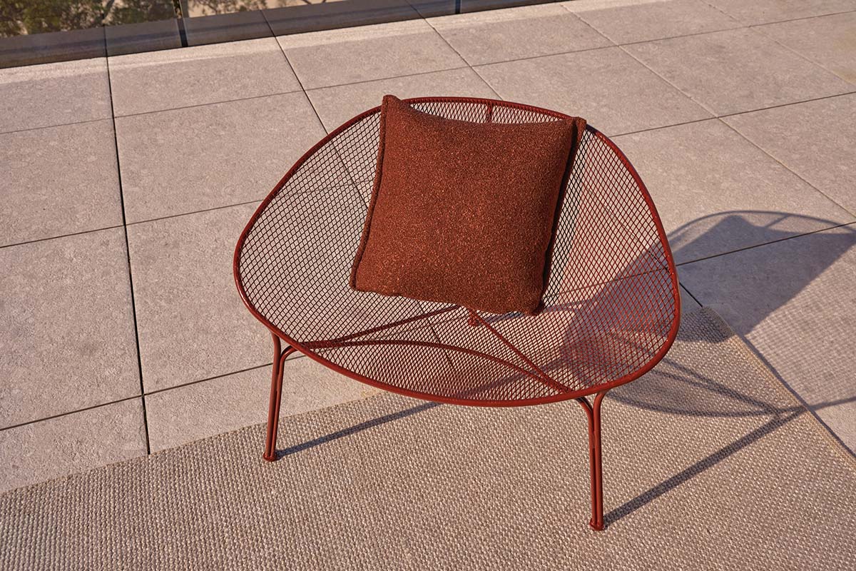 Luna Outdoor Chair in Deep Russet, with a sculptural mesh frame and coordinating cushion on a sunlit terrace.