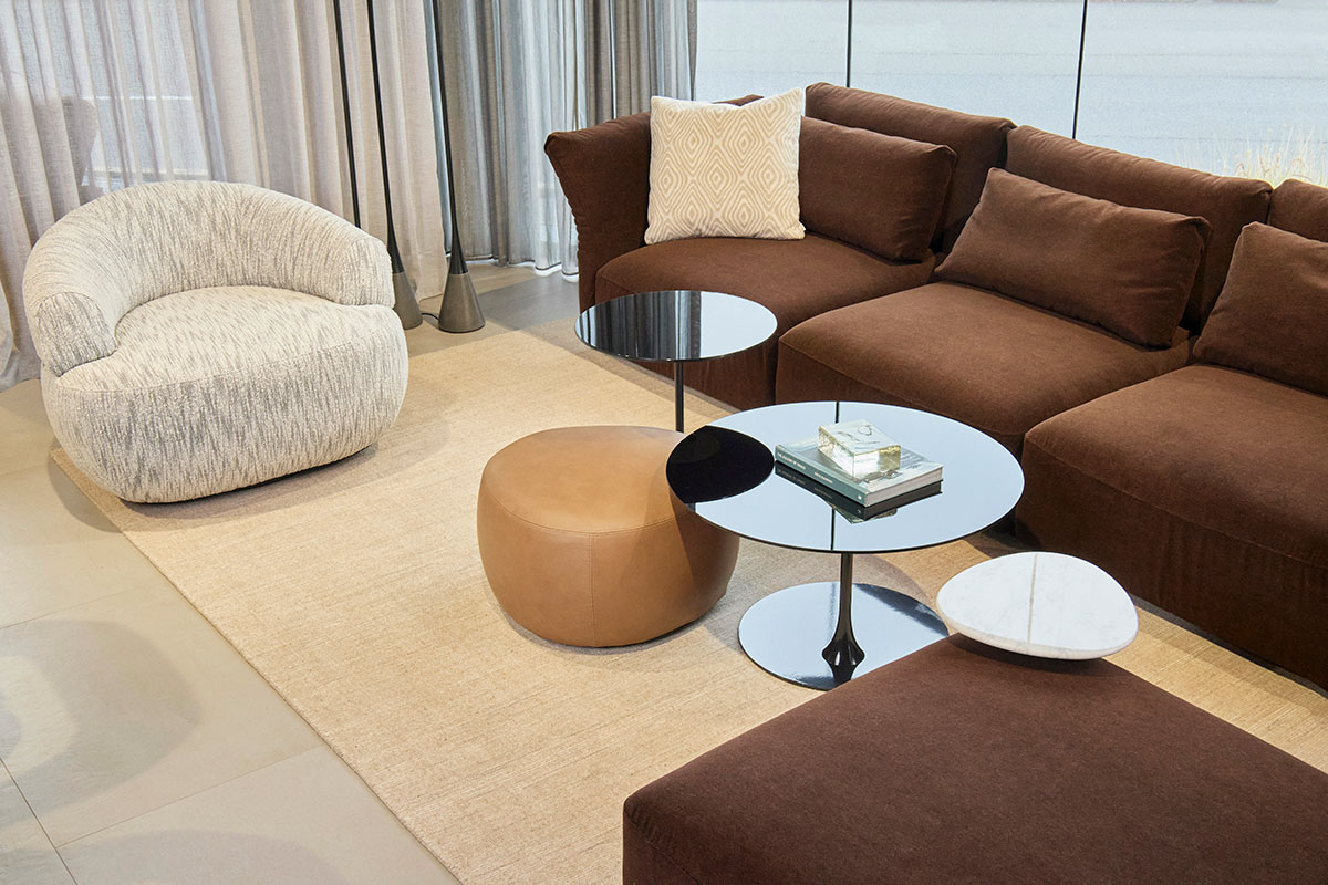 A layered living room setting featuring chocolate brown sofa, tonal brown ottoman and rugs and glass coffee tables.