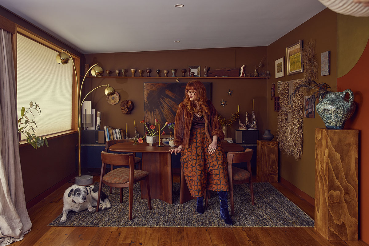 Ruby stands in front of walnut timber dining furniture in her colour drenched chocolate brown and amber dining room.