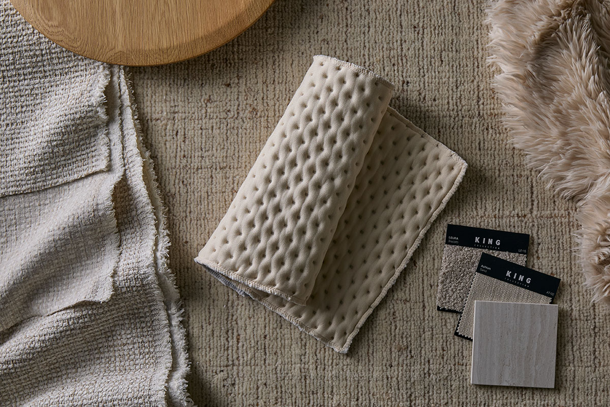 An arrangement of textured fabric swatches in soft, neutral tones, placed on a woven rug.